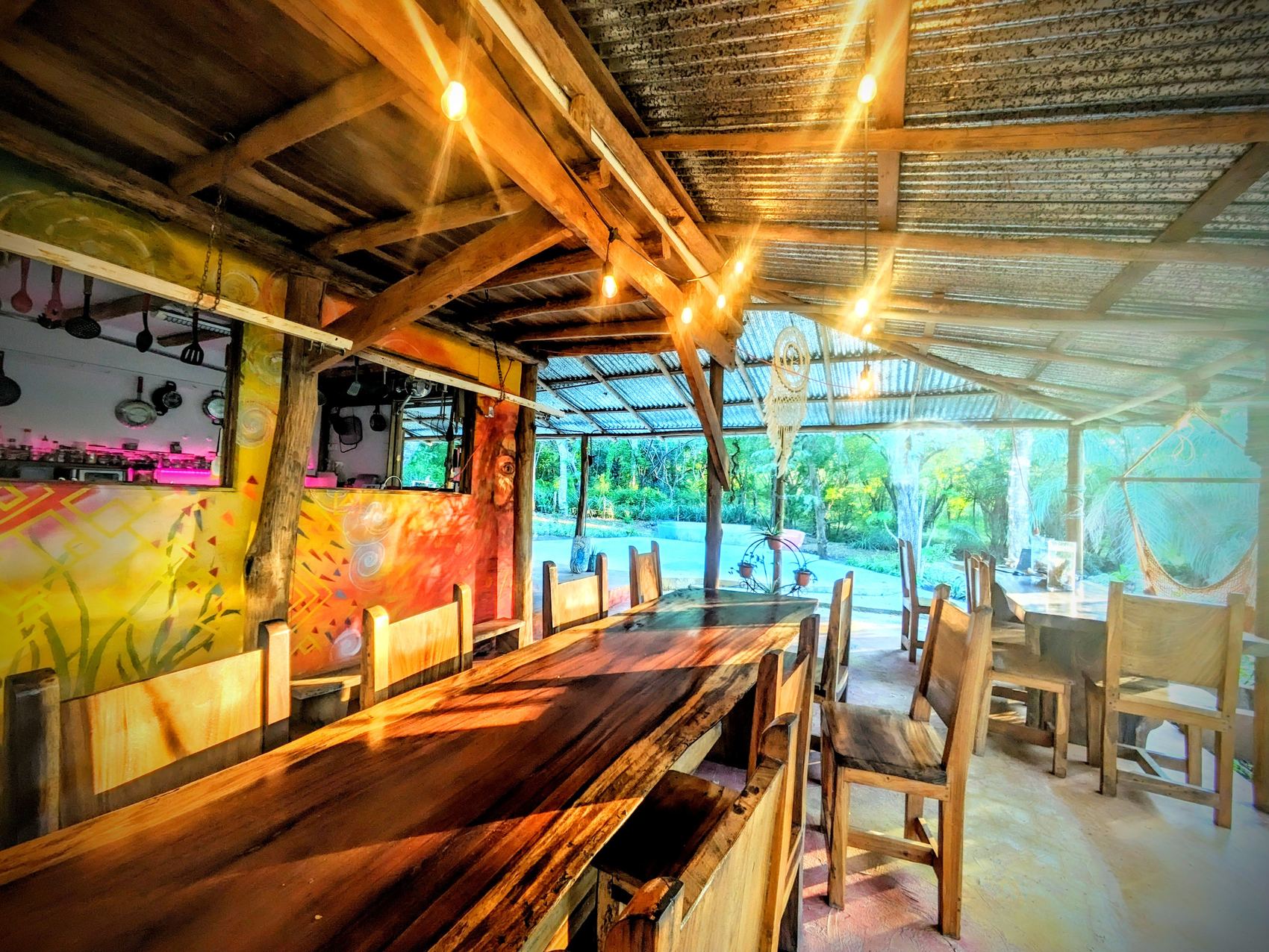 The long live-edge timber table under the covered terrace at sunset, the open kitchen behind.