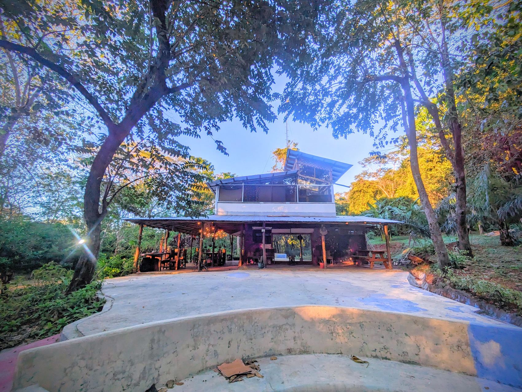 The house at dusk from the concrete apron, showing the covered ground floor and glazed upper storey.